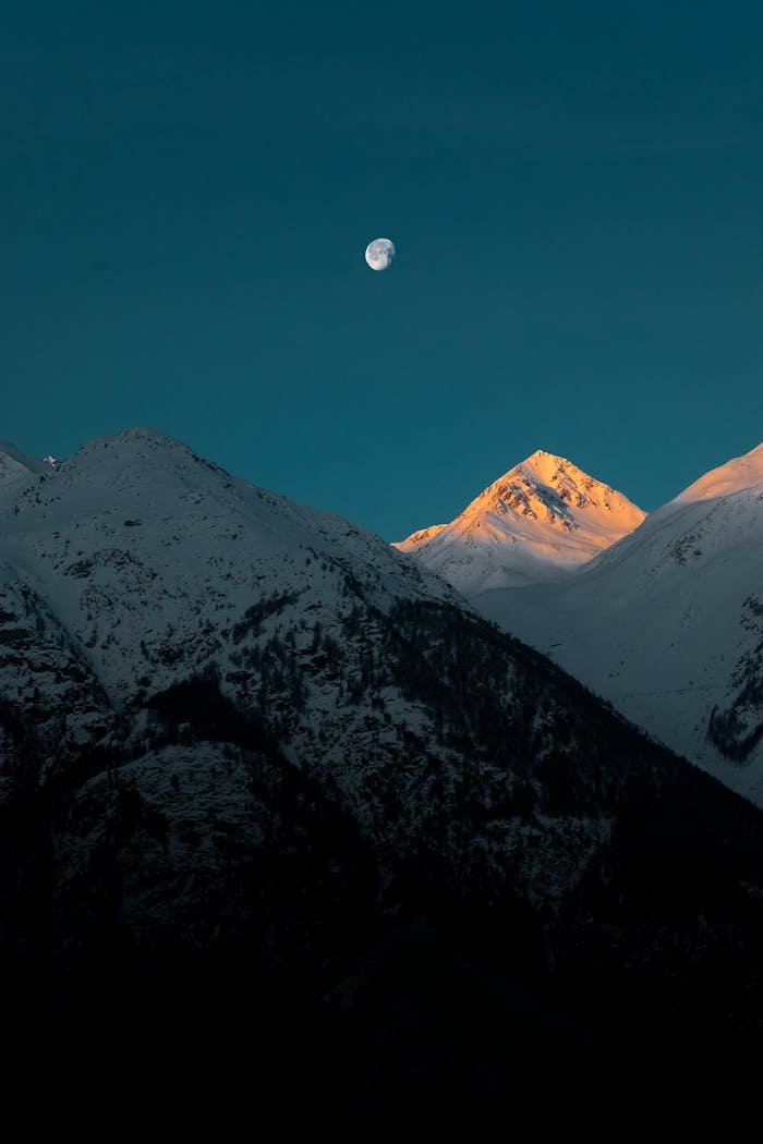 Breathtaking view of a snow-capped mountain peak under the moonlight at twilight.